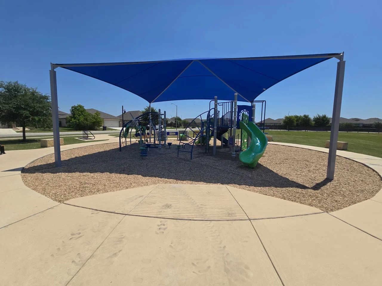 Completed blue shade structure over a community playground after engineered wood fiber surfacing work.